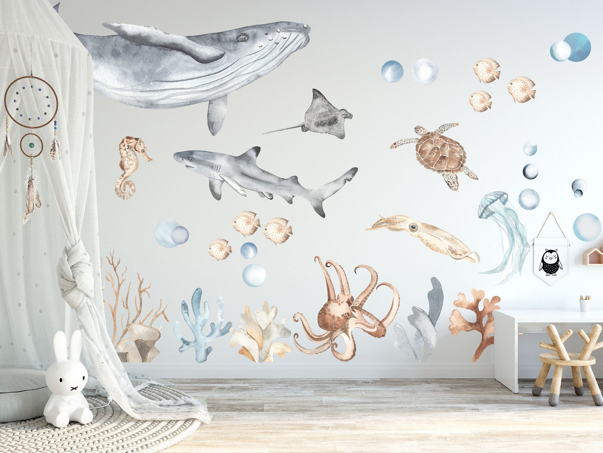 Nursery wall decorated with ocean life fabric decals, including a whale, shark, turtle, jellyfish, squid, coral, and fish, creating a serene underwater scene in pastel watercolors.