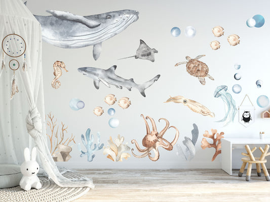 Nursery wall decorated with ocean life fabric decals, including a whale, shark, turtle, jellyfish, squid, coral, and fish, creating a serene underwater scene in pastel watercolors.